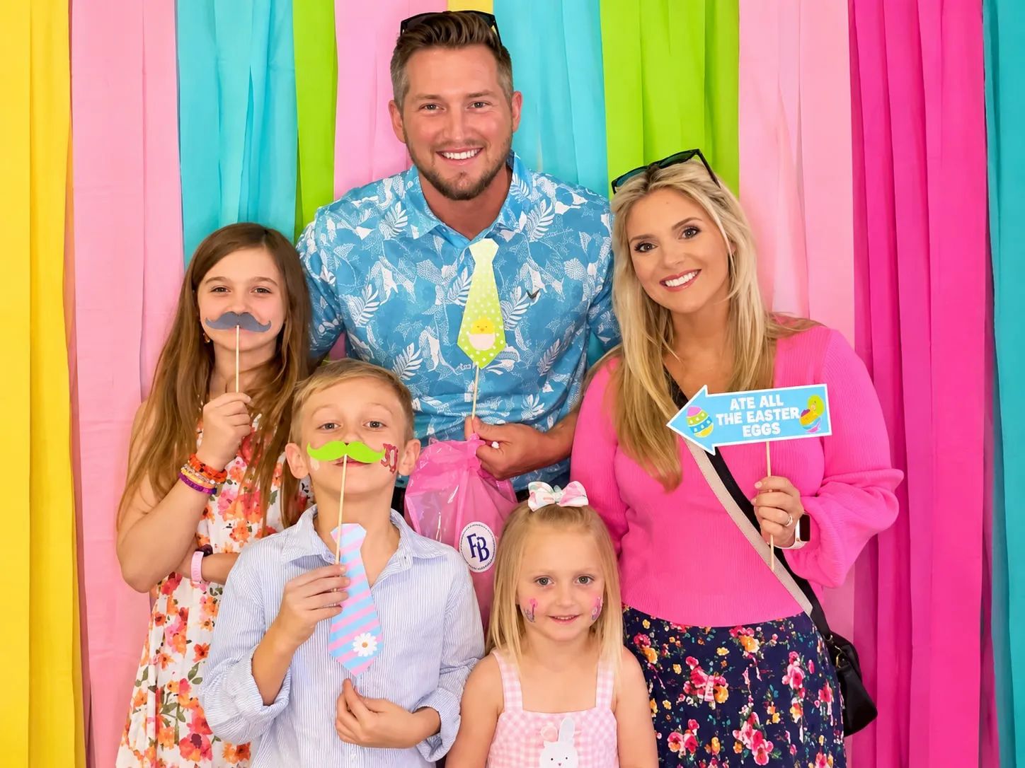 A family holding novelty moustaches and speech bubble signs against a wall of bright pastel streamers