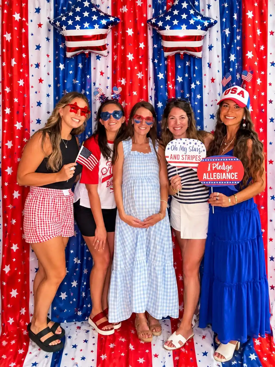 Five friends at a Fourth of July party holding small flags and hand held signs in front of a red, white and blue streamer wall